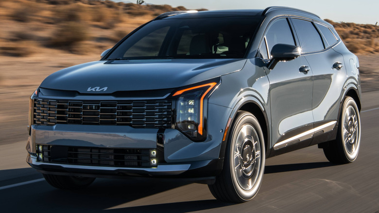 A steel-blue 2026 Kia Sportage HEV crossover SUV cruising along an open desert highway.