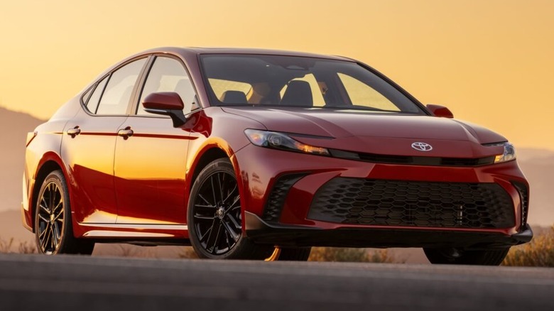A glossy Supersonic Red 2026 Toyota Camry SE AWD sedan parked on an asphalt road during a sunset.