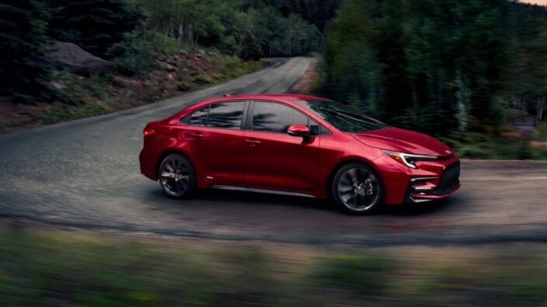 A metallic red 2026 Toyota Corolla Hybrid SE AWD navigates a sharp, sweeping curve on a mountain road.