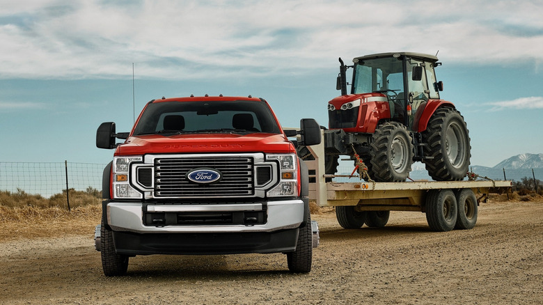 A full frame Ford Super Duty towing a large farm tractor on a gooseneck trailer.