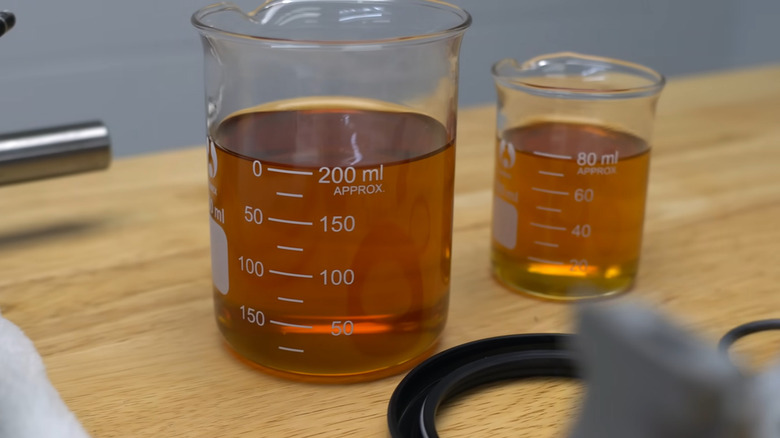 Two beakers filled with full synthetic and high-mileage oil on a table