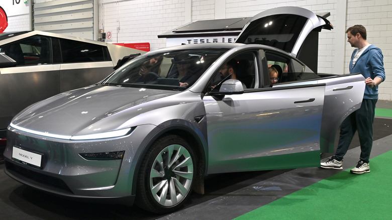A family checking out a silver Tesla Model Y, with all doors open including the rear hatch.