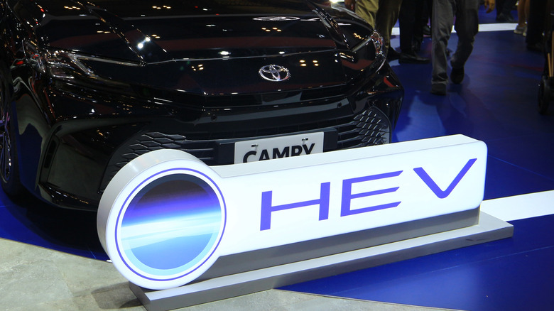 A giant Toyota HEV sign (hybrid electric vehicle) in front of a Camry at an auto show.