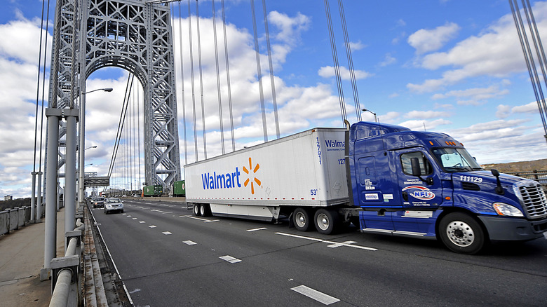 A blue semi truck towing a WalMart trailer across a bridge in front of a cloudy sky