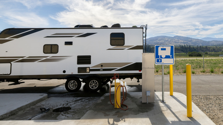 Side view of a travel trailer emptying its tanks properly at an RV dump station
