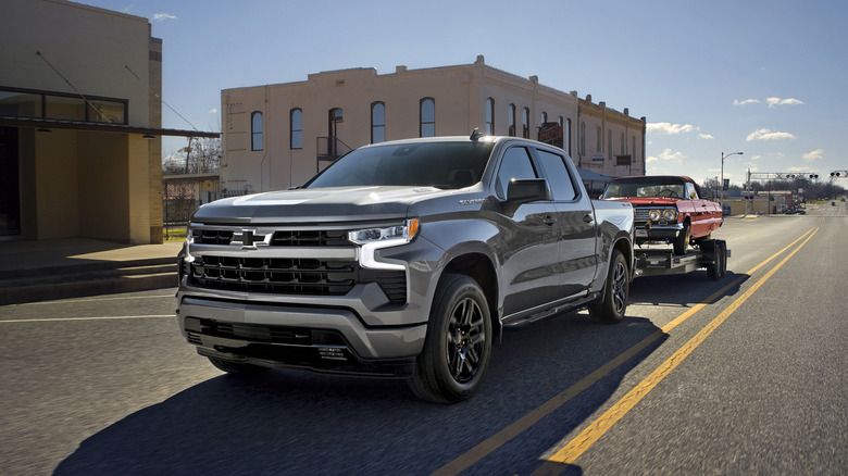 Front 3/4 view of a 2026 Chevrolet Silverado 1500 RST in Sterling Gray Metallic towing a vintage car down a road