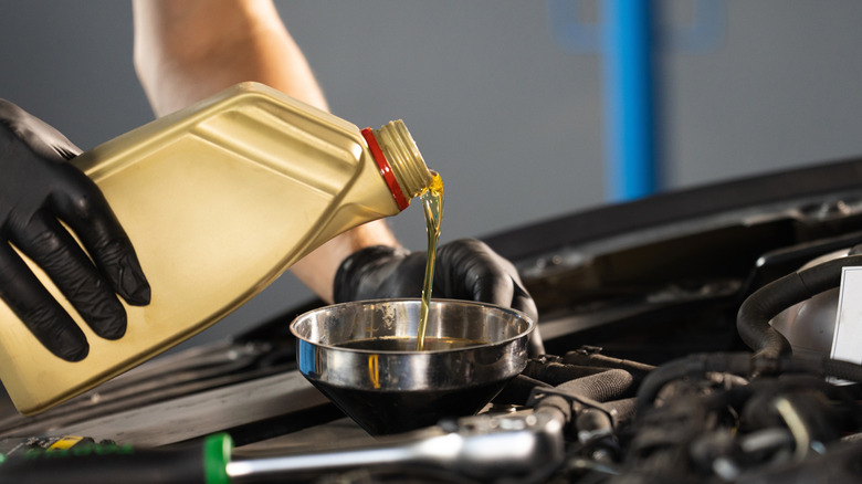 A close up of a person pouring fresh new motor oil into a car's engine