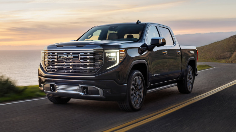 Front 3/4 view of a GMC Sierra Denali driving by the ocean at sunset