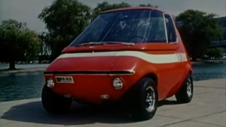 The 1969 GM XP 512E, orange with a white stripe, parked next to water