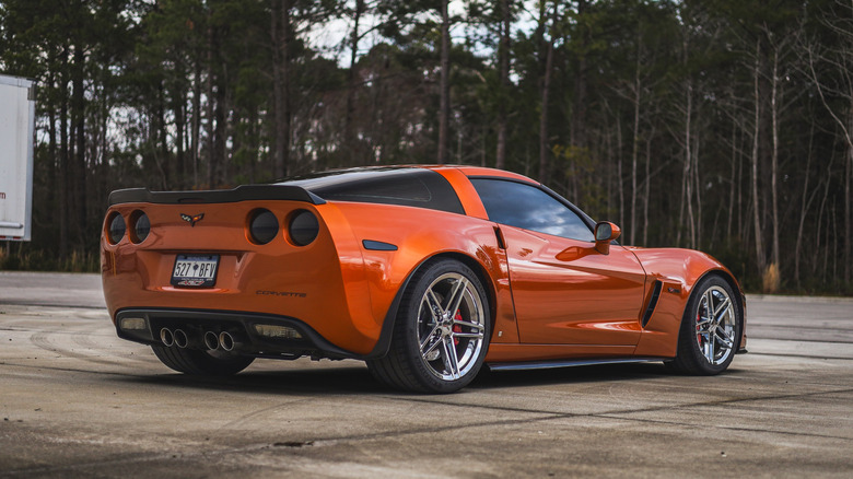 A rear three-quarter view of a chrome orange Corvette with chrome silver wheels and trees in the background.