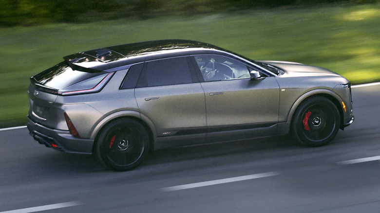 A side view of a dark gray Lyriq V driving next to grass