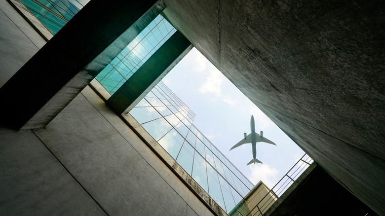 Looking up at an airplane in flight from a glass and concrete building