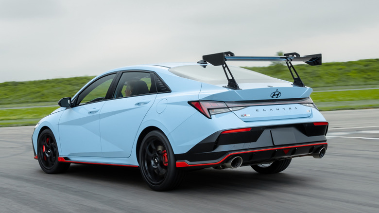 Rear three quarters shot of a blue Elantra N TCR driving on a race track in front of grass showing its massive rear wing