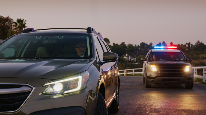 A silver SUV is pulled over by a dark-colored police SUV during a traffic stop at dusk.