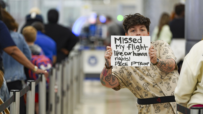 A traveler holds a sign that reads, "Missed my flight like our human rights! F ICE F TRUMP"