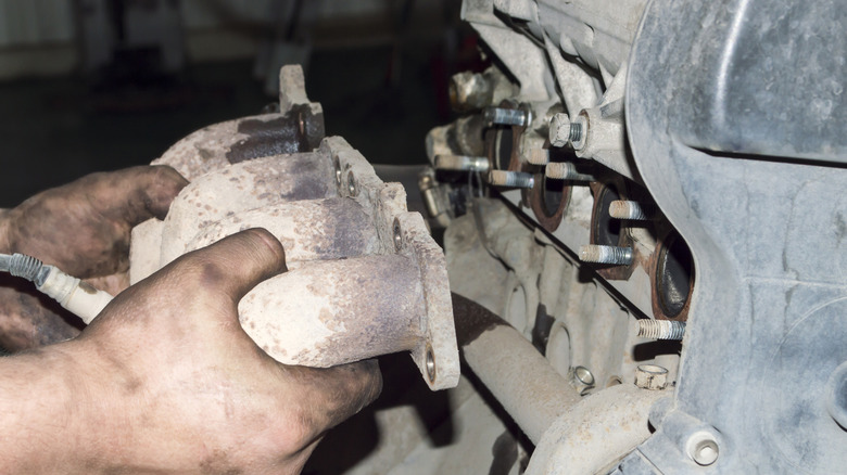 A mechanic removes the exhaust manifold from an automobile internal combustion engine in an auto repair shop