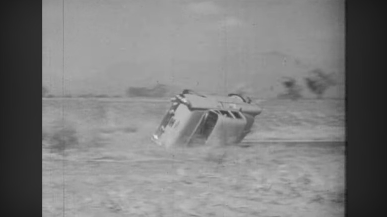 A car on its side after avoiding a crash, it rolls over onto the grass beside the roadway. In black and white.