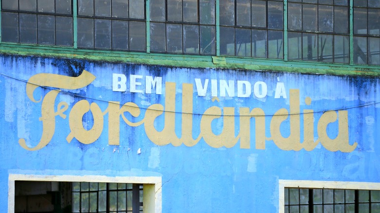 Scripted font reads "Bem vindo &agrave; Fordlandia" on the side of a crumbling blue building from the 1920s.