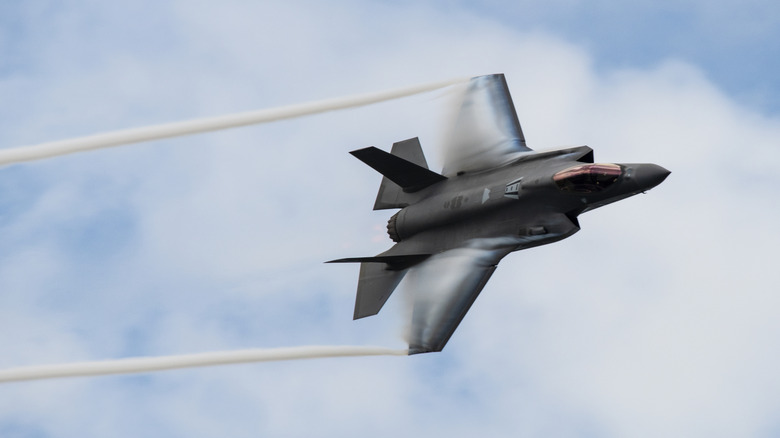 An F-35A flying against a blue sky with vapor trails coming off the wingtips