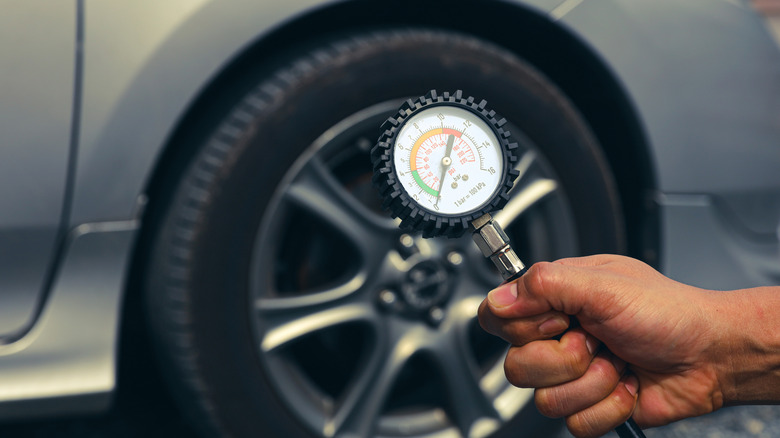 A person holding an air pressure gauge with a tire in the background