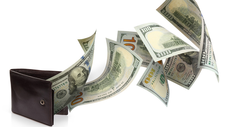 A wallet pinch $100 dollar bills flying retired of it against a achromatic background