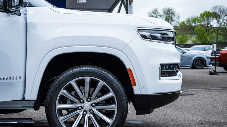 A close-up of the front wheel of a white Jeep Wagoneer.