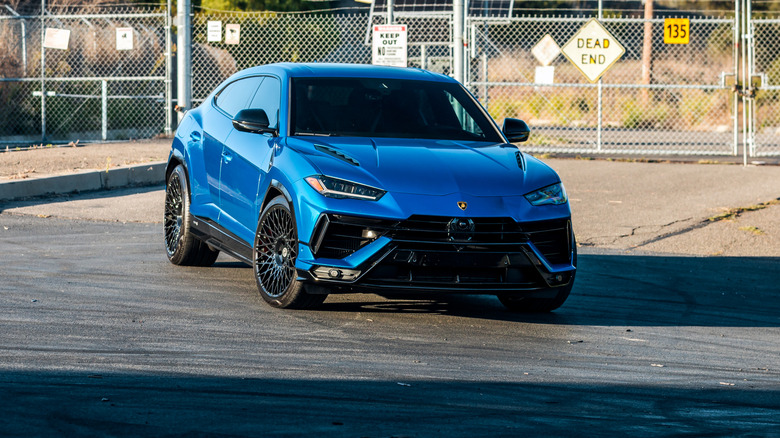 A blue Lamborghini Urus in front of a fence.
