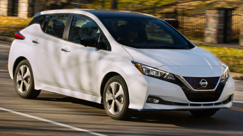 A 2020 Nissan Leaf driving on a paved road next to a hillside
