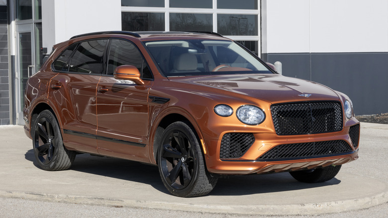 A metallic orange 2021 V8 Bentley Bentayga parked in front of a building.