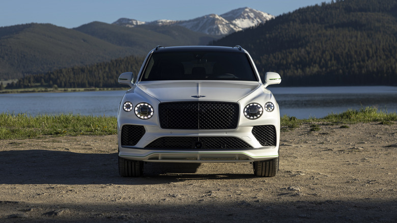 A front-end shot of a white Bentley Bentayga parked in front of a body of water.