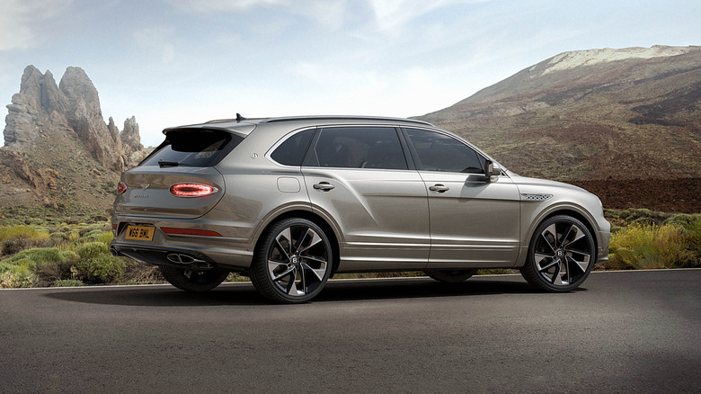 A rear three-quarter shot of a gray Bentley Bentayga with a roof rack parked in front of a mountain range.