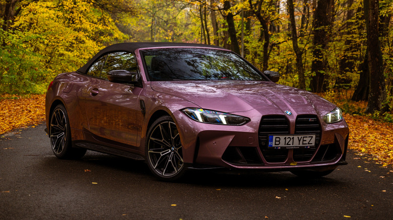 A purple G82 BMW M4 Convertible parked in the middle of a country road in an autumn setting.