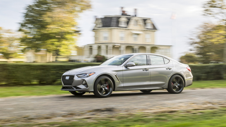 A silver 2021 Genesis G70 in motion in front of a house.