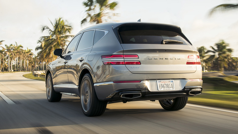 A gray 2021 Genesis GV80 seen from behind on a roadway with palm trees in the background.
