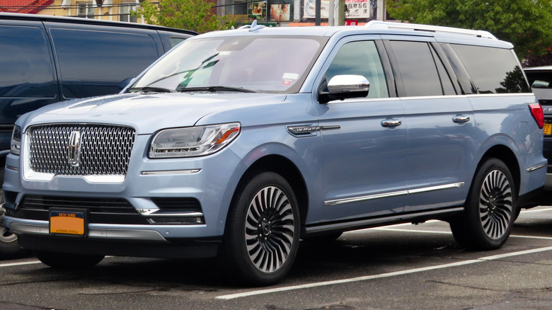 A fourth-generation Lincoln Navigator L parked in a paved lot with other cars in the background
