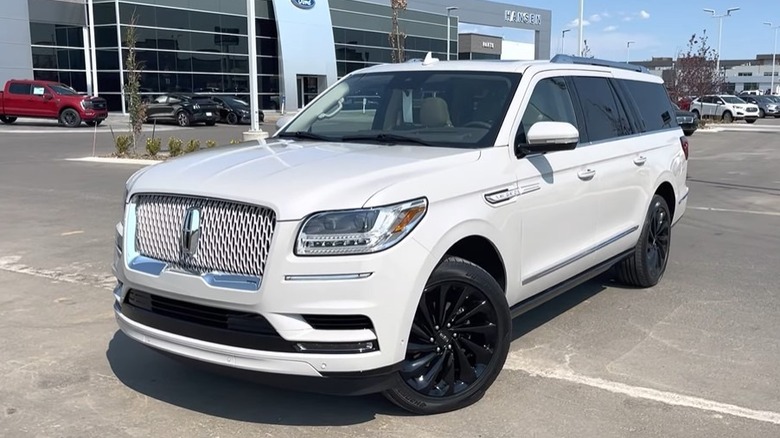A 2021 Lincoln Navigator L parked on a paved surface with buildings and other cars in the background