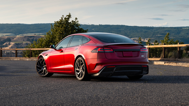 A left and rear quarter view of a red Tesla Model S parked on the middle of a curvy road.