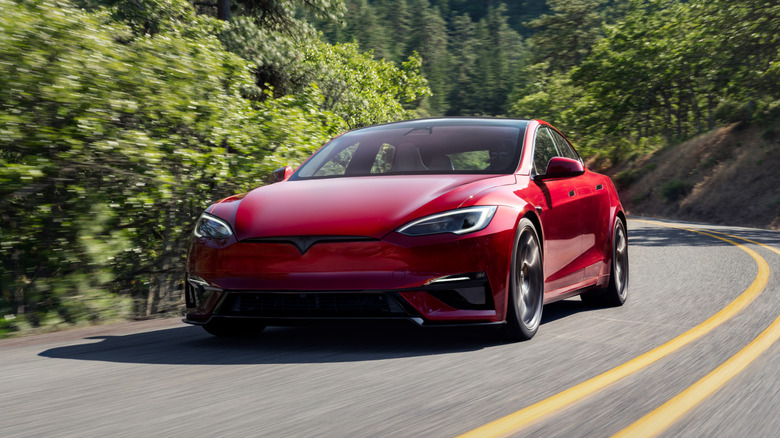 A red Tesla Model S moving swiftly on a curvy mountain road