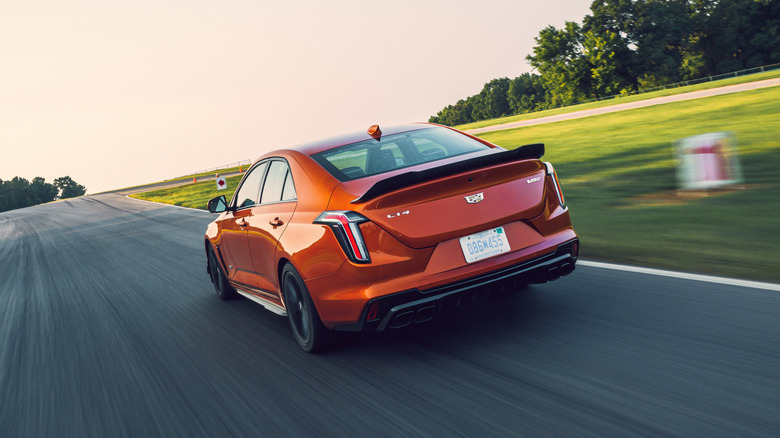 A rear left 3/4 of an orange 2022 Cadillac CT4-V Blackwing on a racetrack.