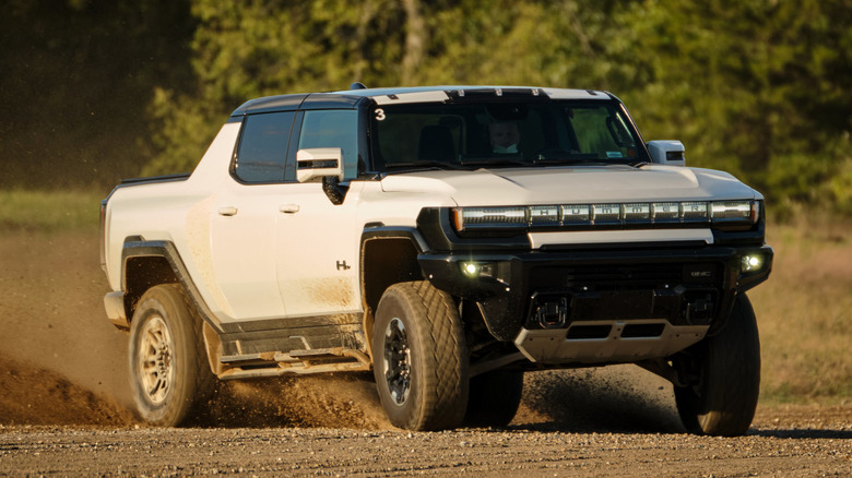 A white 2022 GMC Hummer EV pickup in motion on an unpaved surface.