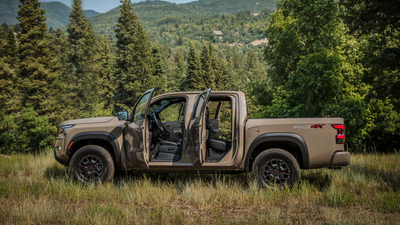 A side-profile shot of a tan 2022 Nissan Frontier parked in a forest with all of its doors open