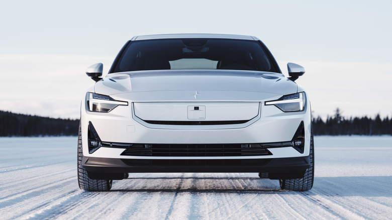 A front-end face view of a white Polestar 2 EV parked in wintery conditions.