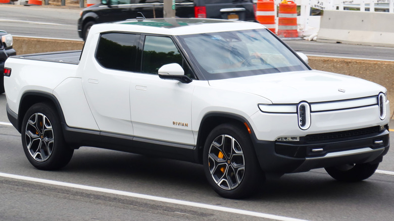 A white 2022 Rivian R1T driving on a paved road with other vehicles in the background