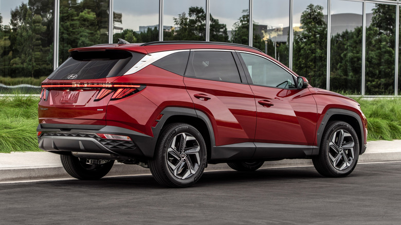 A rear 3/4 view of a 2023 Hyundai Tucson parked in front of a glass building