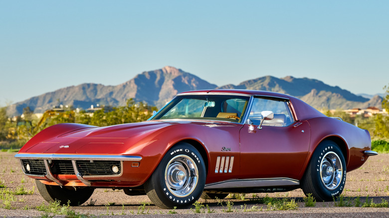 A red Chevy C3 Corvette parked outside with mountains in the background