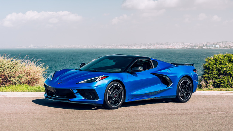 A blue Chevrolet C8 Corvette parked outside with water in the background