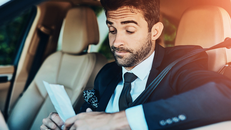 Man in a vehicle looking at a speeding ticket.