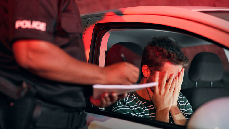 Man covering his face with his hands, with police officer writing a ticket.