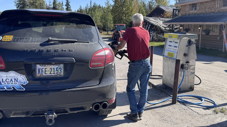 An old man pumping diesel into a Porsche Cayenne