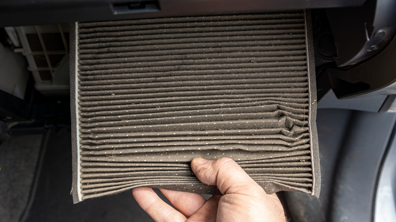A mechanic removing a dusty gray cabin air filter from the glovebox of a car